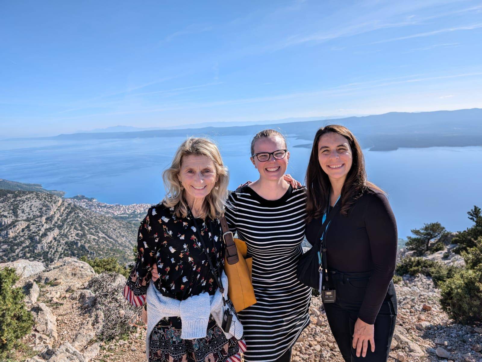 A group of three women poses joyfully for a photograph on a mountain.