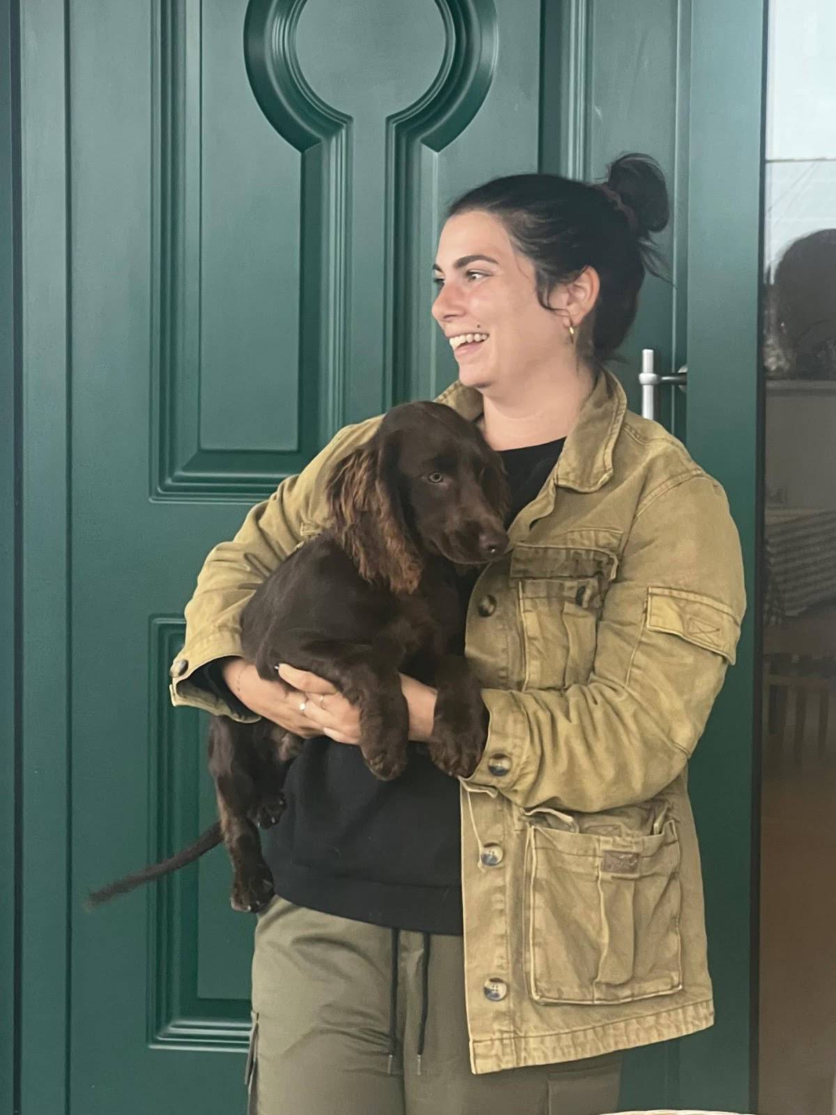 A woman cradles a brown dog in her arms, standing in front of a vibrant green door.