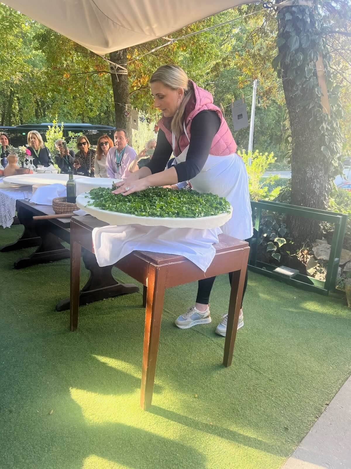 A woman is skillfully preparing food on a table set outdoors, surrounded by nature and natural light.