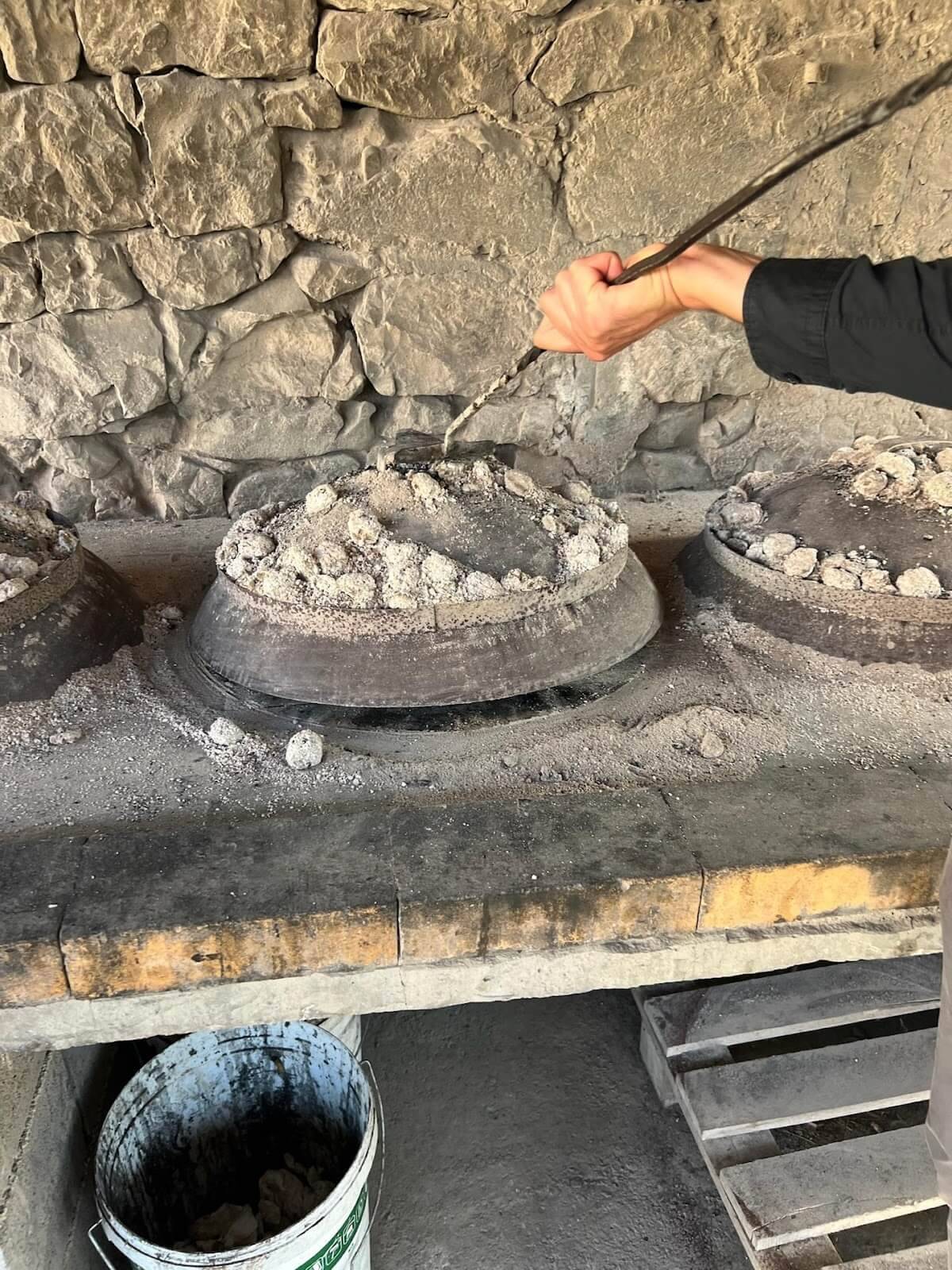 A woman is engaged in the art of pottery, molding clay pots within a traditional stone oven setting.