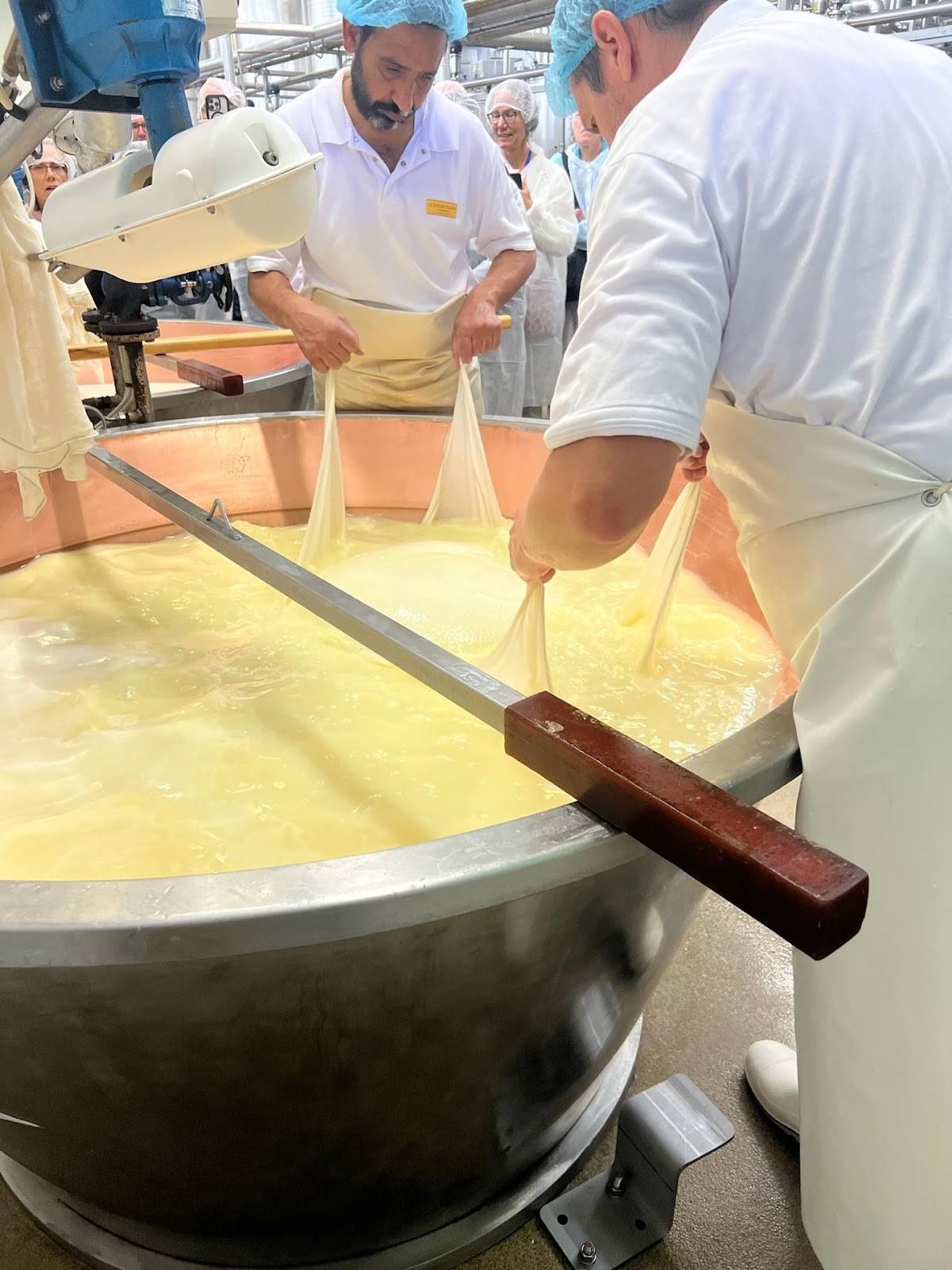 Two men in white aprons are skillfully preparing cheese in a large bowl, showcasing their culinary expertise.