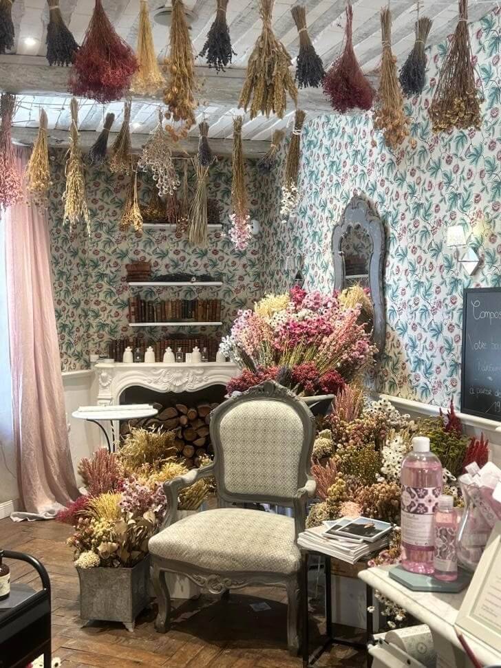 A cozy floral shop featuring dried flowers hanging from the ceiling, a vintage chair, and a stylish decor with a warm ambiance.