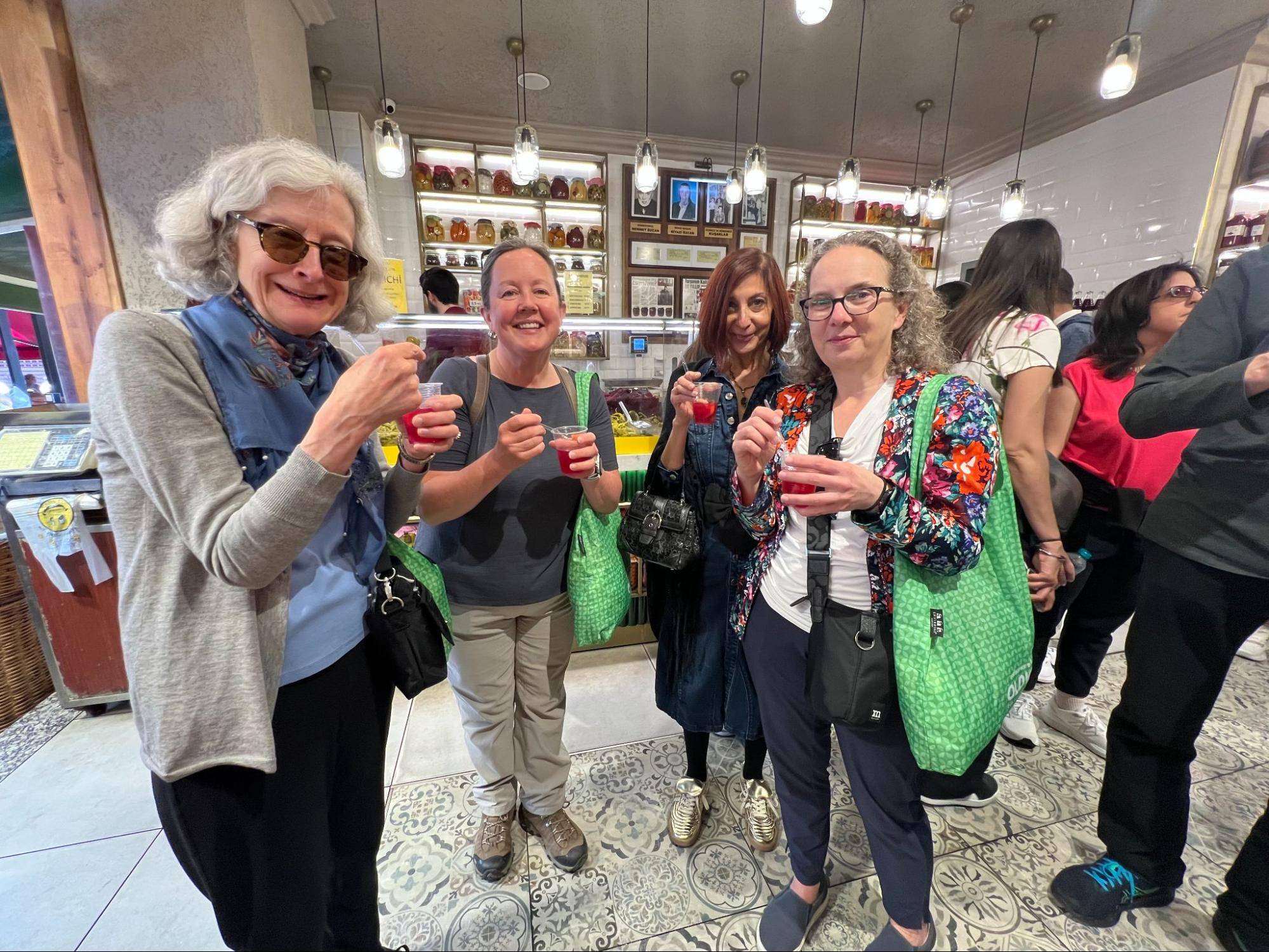 A group of four people enjoy drinks in a vibrant, busy store with jars lined on the shelves in the background.