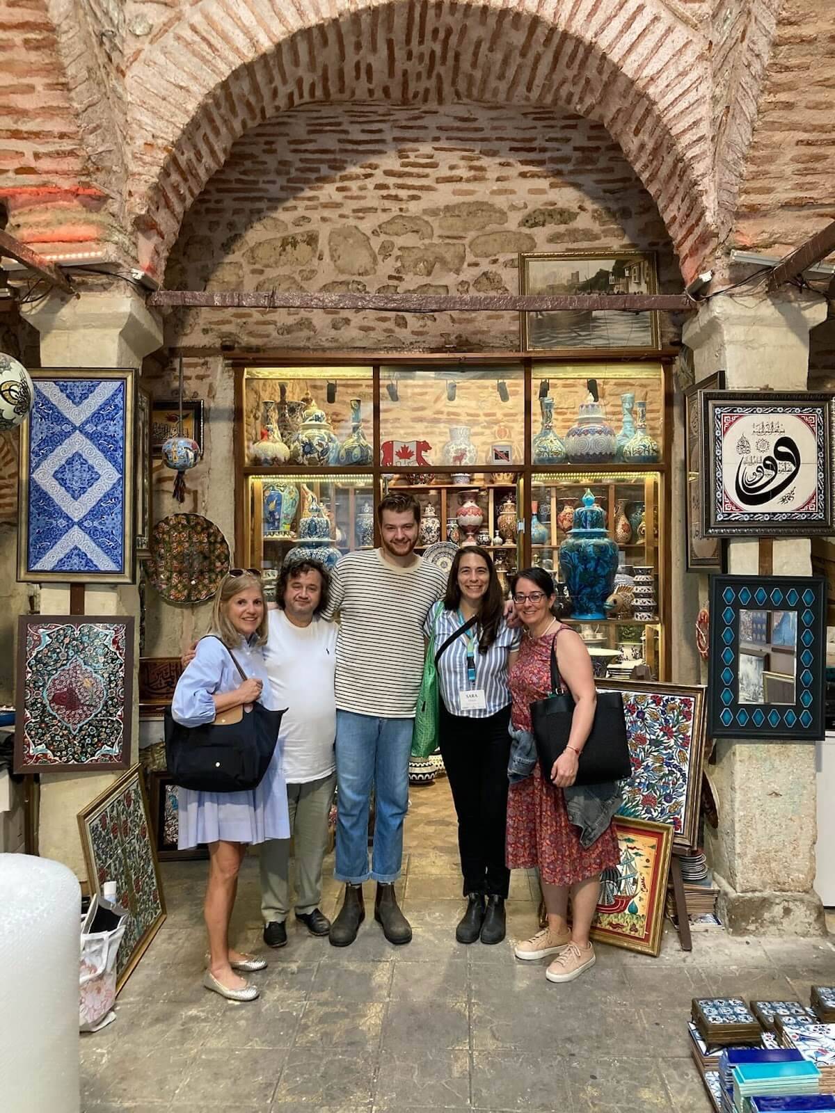A diverse group of people stands together in front of a store, smiling and engaging with one another.