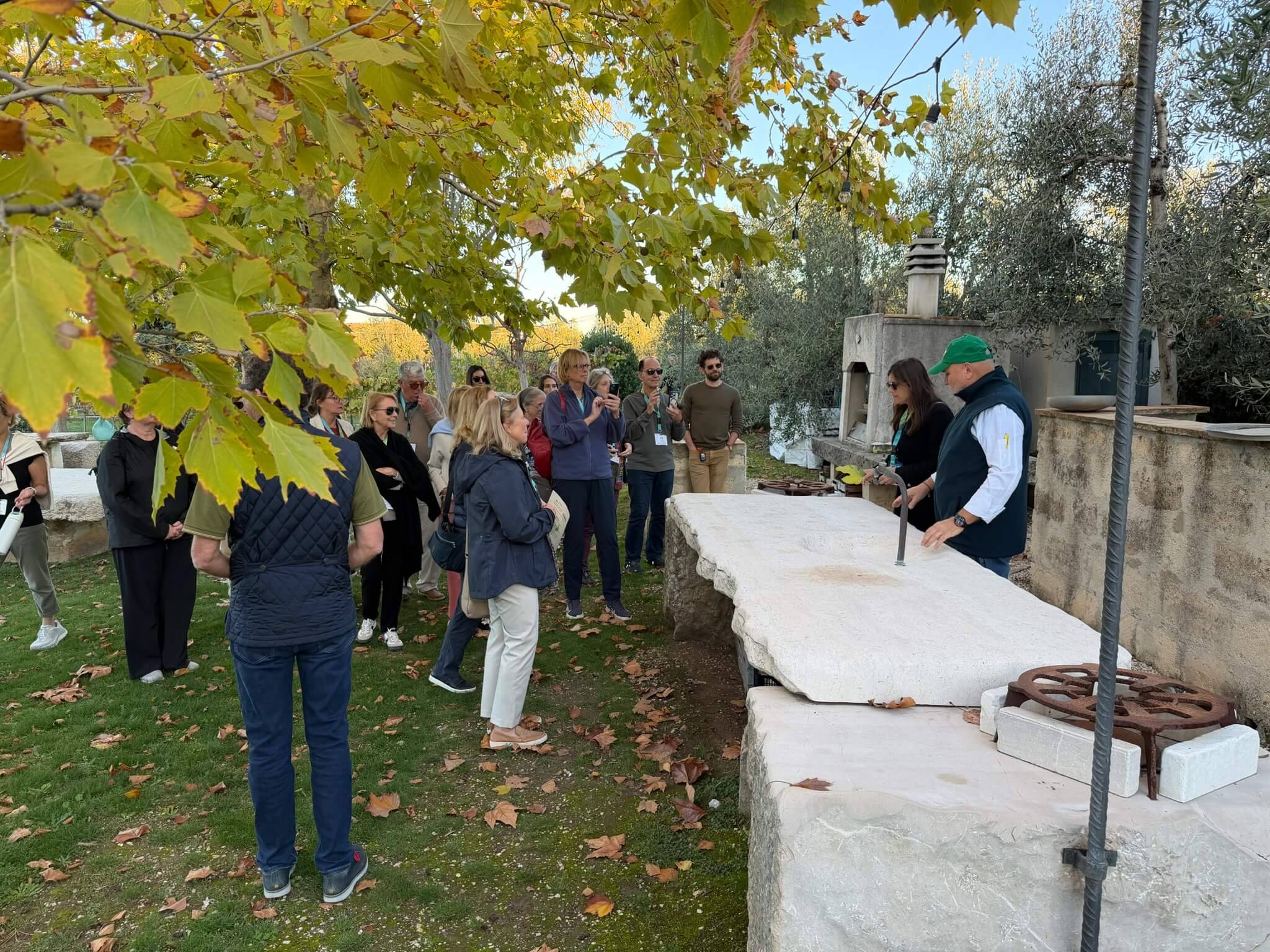 Group observing outdoor stone structure with autumn leaves.