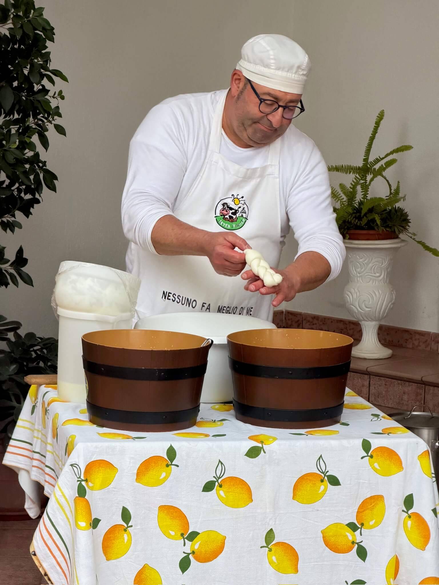 Man shaping dough at an outdoor table with lemon-themed tablecloth.