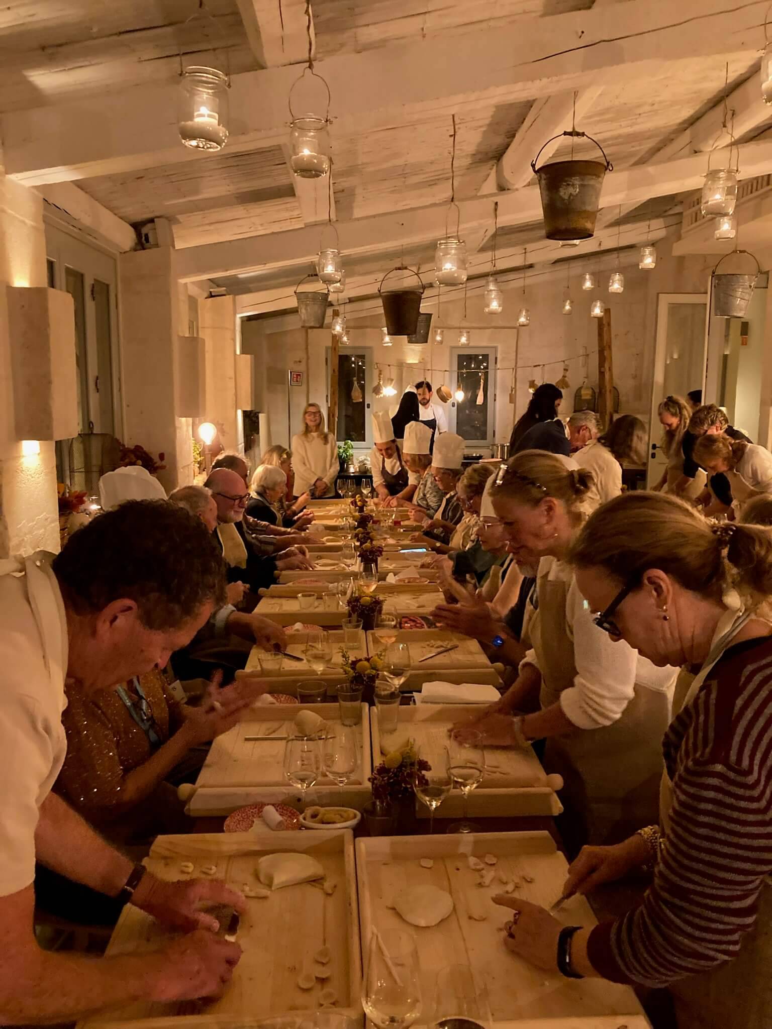 People participating in a cooking class at a long table with aprons, chef hats, and various cooking utensils.