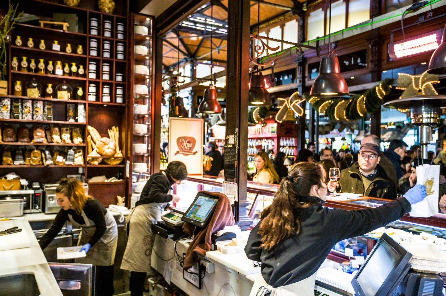 A group of people stands in a restaurant near a counter, engaged in conversation and enjoying the atmosphere.