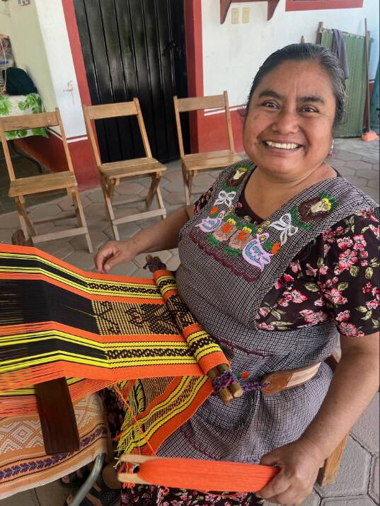 A smiling woman holds a vibrant, colorful woven cloth