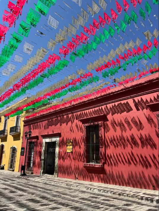 A vibrant street adorned with colorful flags hanging from the rooftops, creating a festive atmosphere.