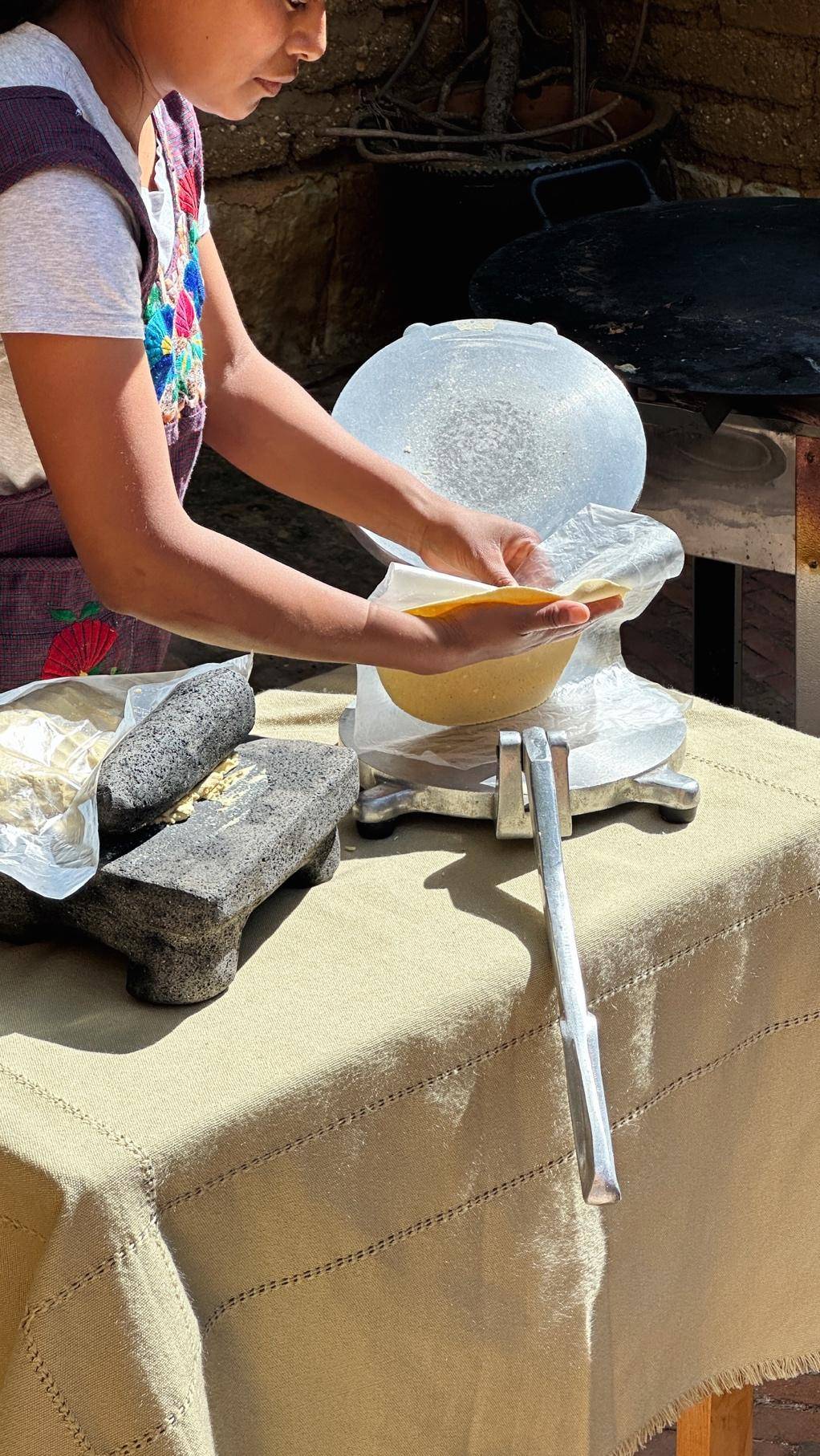 A young girl is focused on preparing food at a table, surrounded by ingredients and cooking utensils.