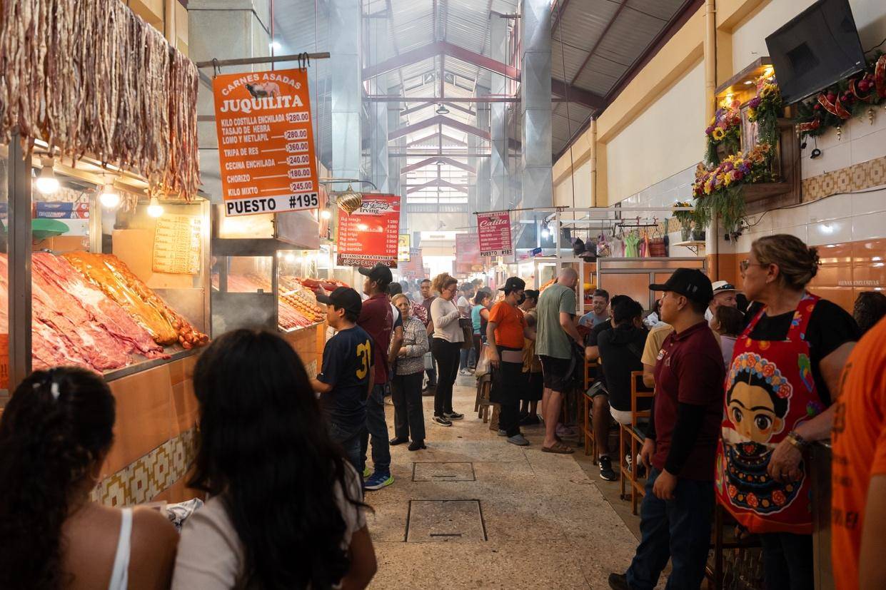 A bustling market scene with shoppers browsing various meat displays and interacting with vendors.