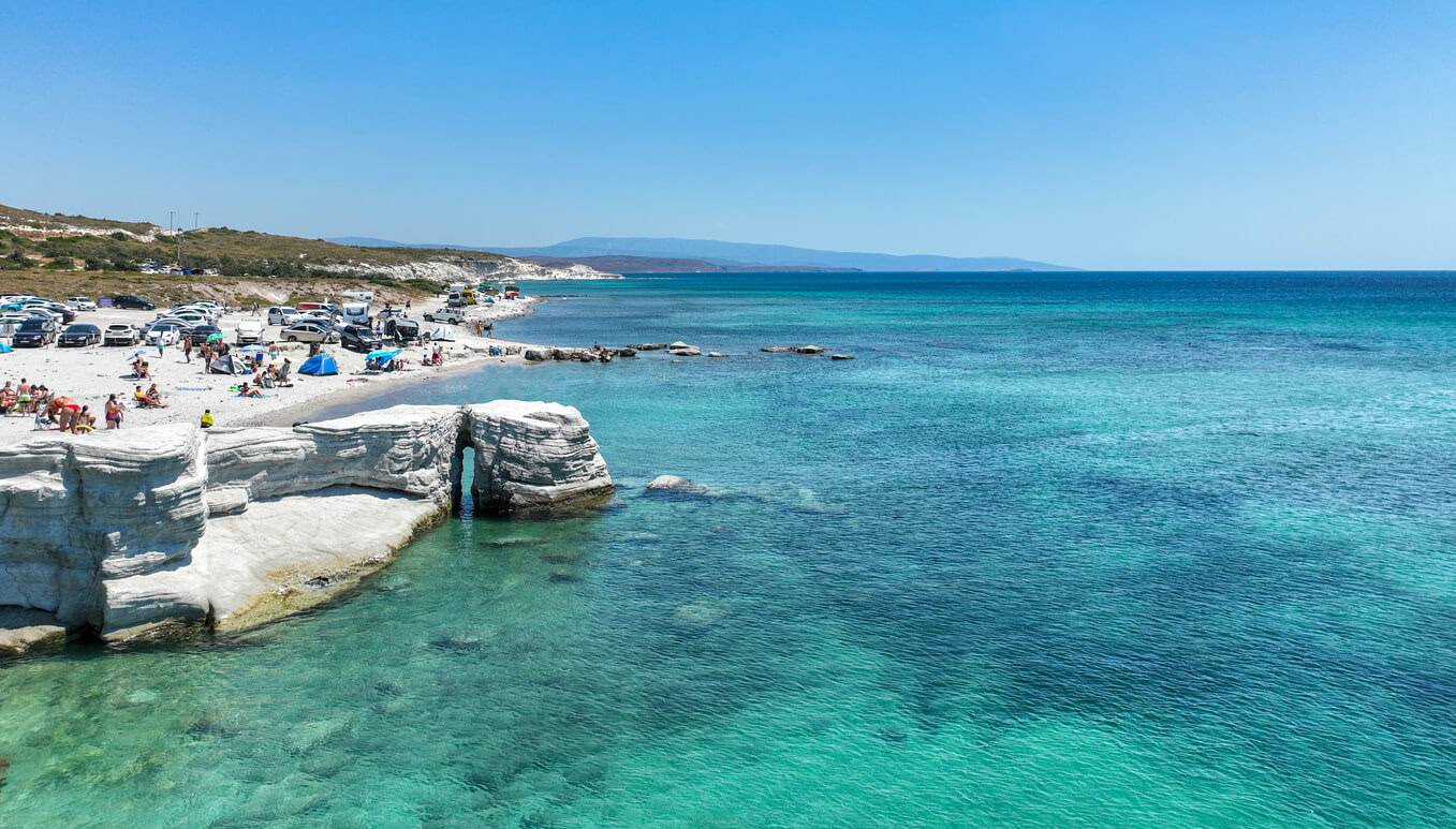 A scenic view of the beach on the island of Kos, Greece, featuring golden sand and clear blue waters under a sunny sky.