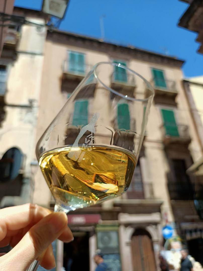 A hand holds a glass of white wine up to a blue sky