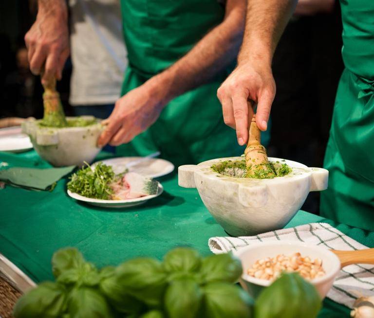 Two chefs in green aprons prepare food on a table