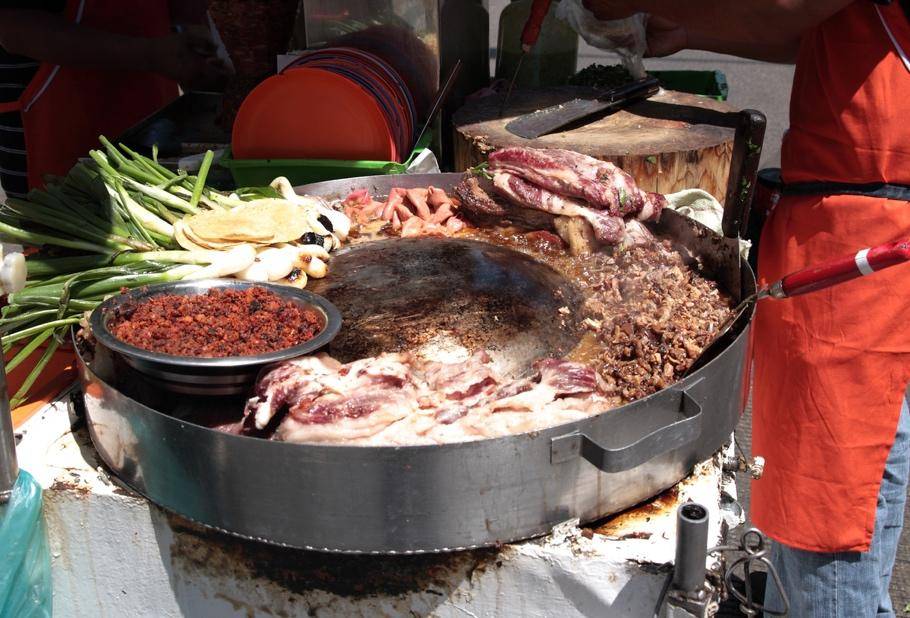 A street food vendor prepares tacos on a round grill