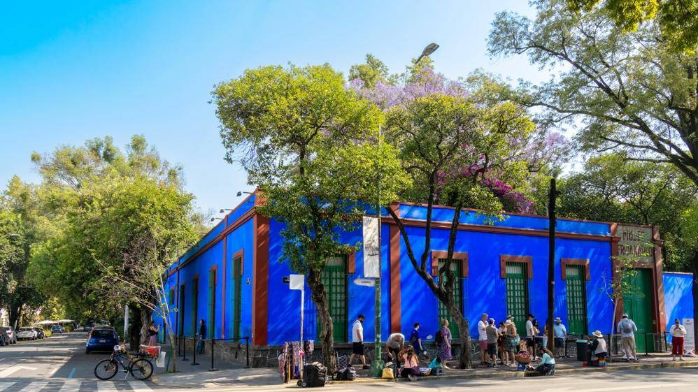 Bright blue corner building with red trim and green windows, surrounded by trees