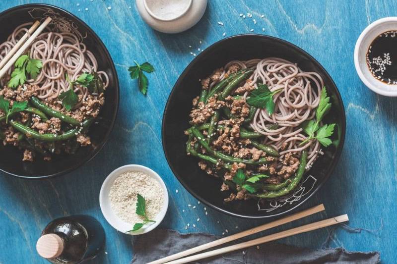 Two black bowls of soba noodles topped with minced meat