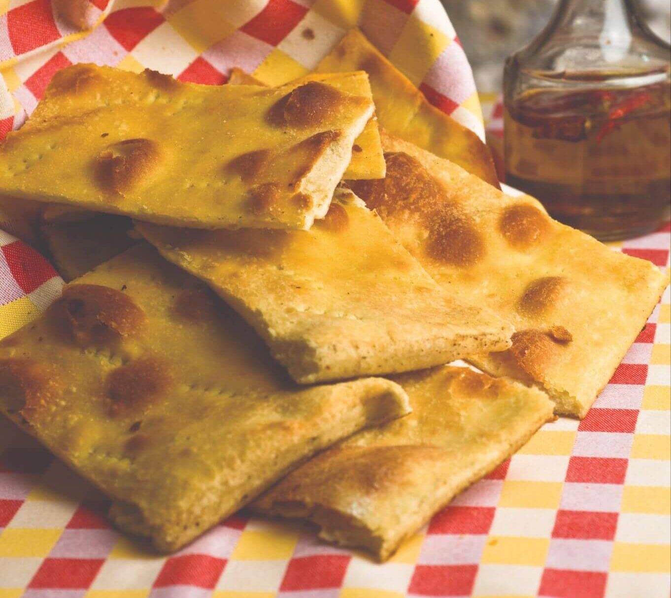 A stack of flatbreads rests on a red and white checkered tablecloth